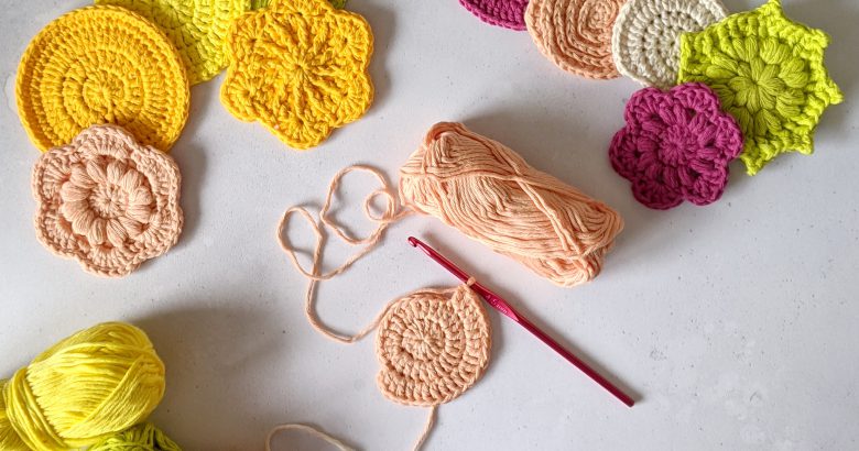 Ten finished crochet face scrubs in round and flower shapes made in yellow, green, peach and pink yarn. There is also a face scrub in progress