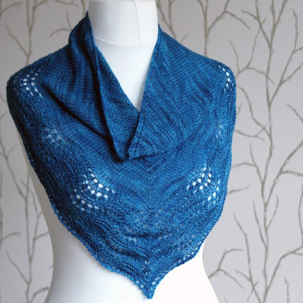 A blue triangular cowlette with a stocking stitch body and rippling lace and textured border