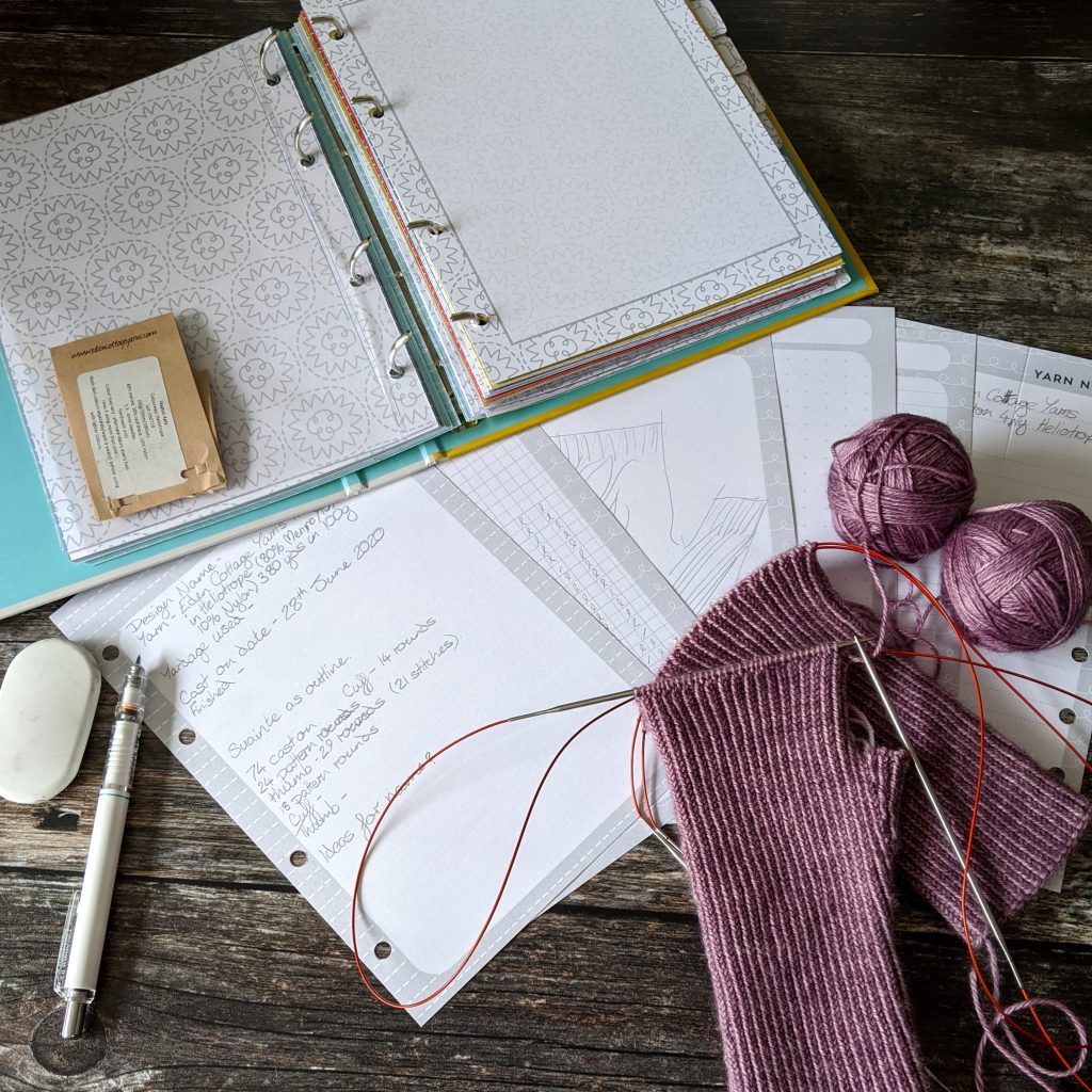 An open ring binder with the pages taken out and a knitting design in progress