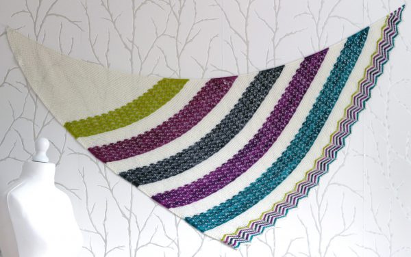 A shawl with coloured lace stripes and chevron border showing the triangular shape