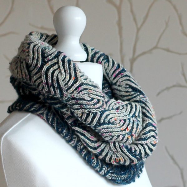 A mannequin displaying a long brioche cowl in blue and white with a owl pattern wrapped twice around the neck