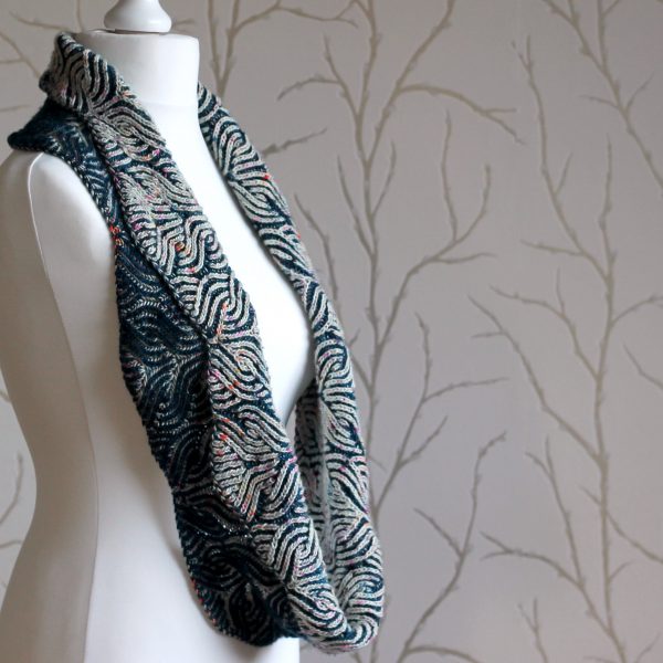 A mannequin displaying a long brioche cowl in blue and white with a owl pattern