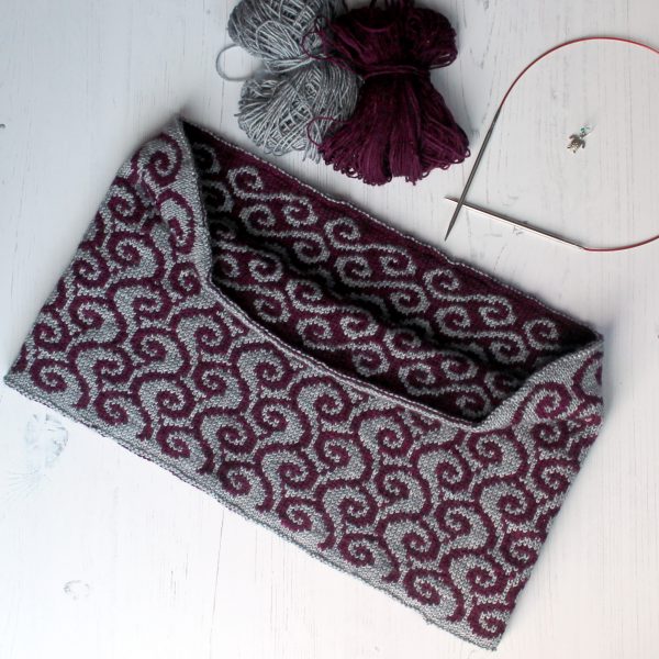 A colourwork cowl with purple waves against a grey background on the outside and grey swirls against a purple background on the inside