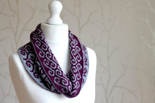 A colourwork cowl with purple waves against a grey background on the outside and grey swirls against a purple background on the inside which has been folded down