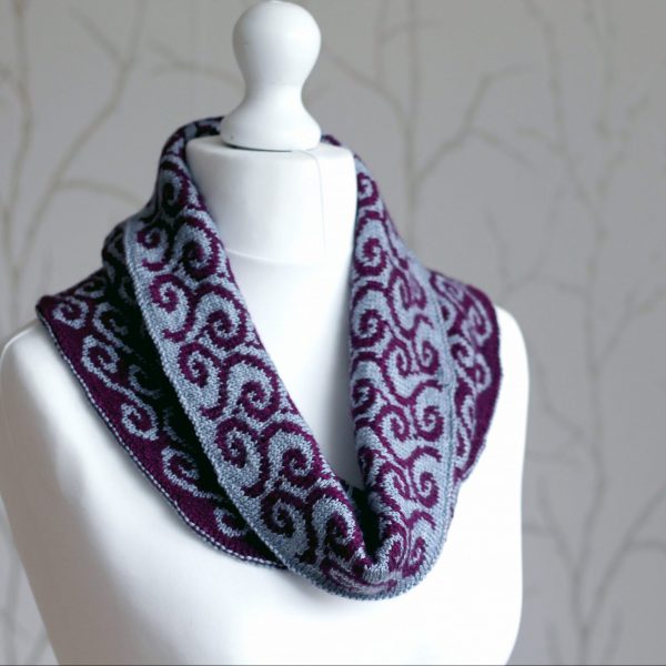 A colourwork cowl with grey swirls against a purple background on the outside and purple waves against a grey background on the inside which has been folded down