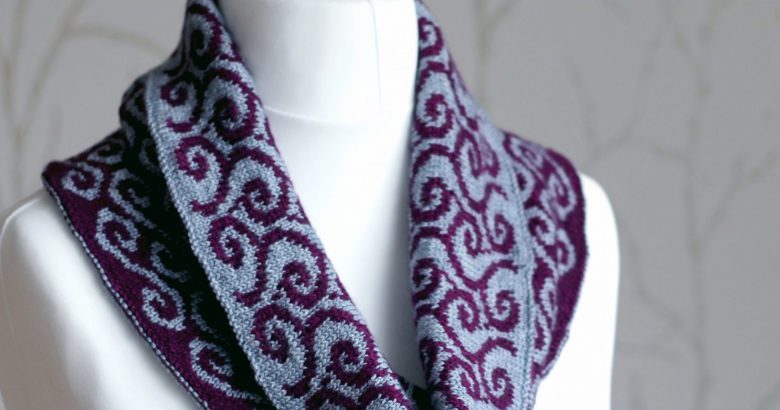 A colourwork cowl with grey swirls against a purple background on the outside and purple waves against a grey background on the inside which has been folded down