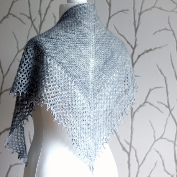 A grey shawlette with a textured body and wide lace border on a white mannequin.