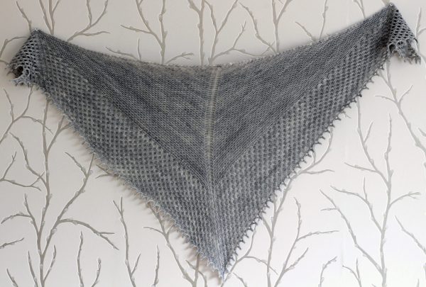 A grey shawlette with a textured body and wide lace border showing the triangular shape.