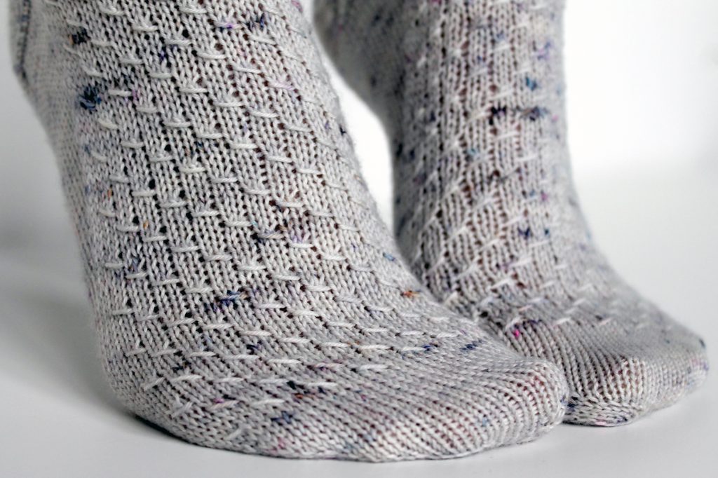 Grey speckled socks with an all-over textured pattern mirrored on each foot