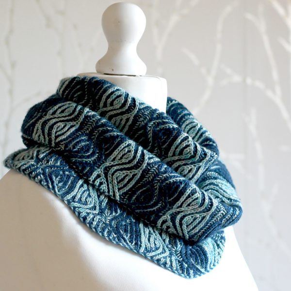 A mannequin displaying a long brioche cowl with dark and light blue vertical stripes and a faux cable pattern wrapped twice around the neck