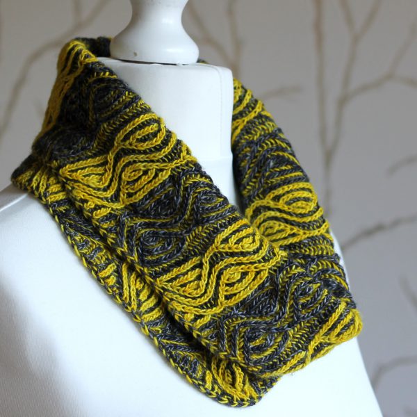 A mannequin displaying a short brioche cowl with grey and yellow vertical stripes and a faux cable pattern