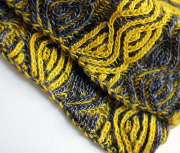 A close up on a brioche cowl with yellow and grey vertical stripes showing the cast-on and bind-off