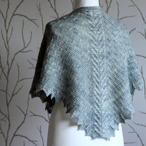 A grey shawl with a cabled spine, a garter stitch body with slipped stitch detail and chevron detail on the edge.