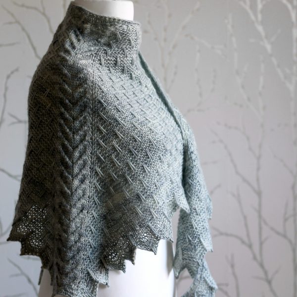 A grey shawl with a cabled spine, a garter stitch body with slipped stitch detail and chevron detail on the edge.