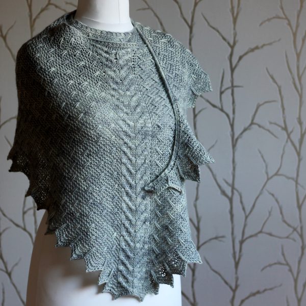 A grey shawl with a cabled spine, a garter stitch body with slipped stitch detail and chevron detail on the edge.