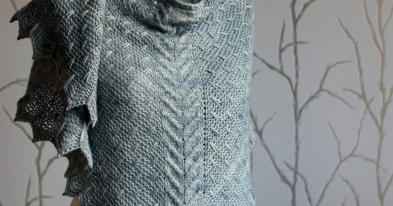 A grey shawl with a cabled spine, a garter stitch body with slipped stitch detail and chevron detail on the edge.