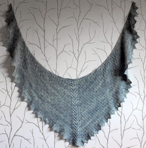 A grey shawl with a cabled spine, a garter stitch body with slipped stitch detail and chevron detail on the edge.