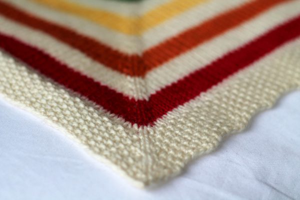 A square baby blanket with rainbow stripes and a seed stitch border