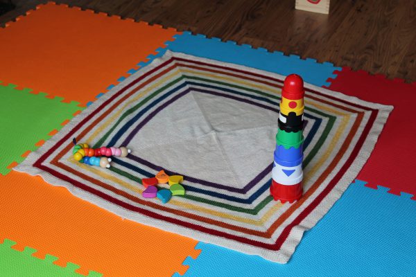 A square baby blanket with rainbow stripes and a seed stitch border