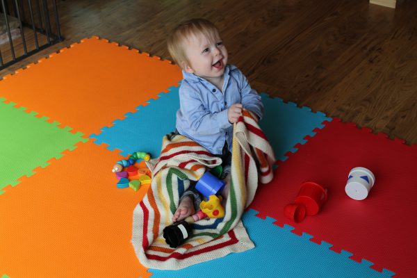 A square baby blanket with rainbow stripes and a seed stitch border