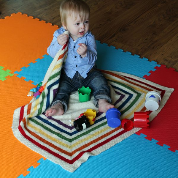 A square baby blanket with rainbow stripes and a seed stitch border