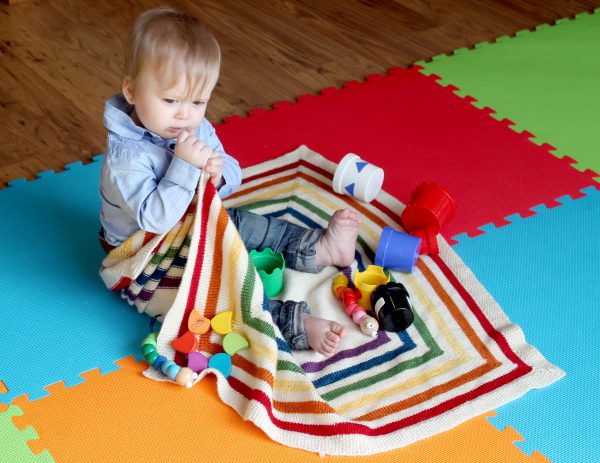 A square baby blanket with rainbow stripes and a seed stitch border