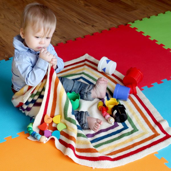 A square baby blanket with rainbow stripes and a seed stitch border