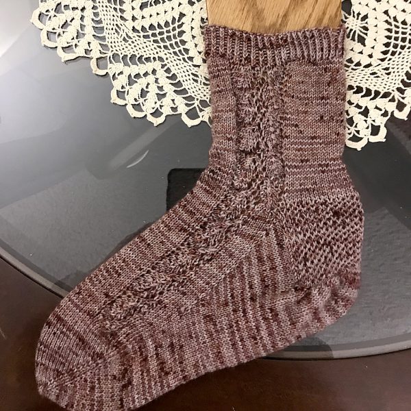 A sock with a lace leaf pattern up the outside of the foot knitted in variegated brown yarn