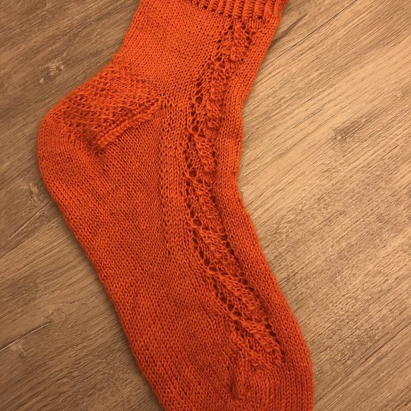 An orange sock with a lace leaf pattern up the outside of the foot