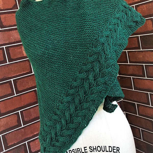 A green triangular cabled shawl draped over a mannequin