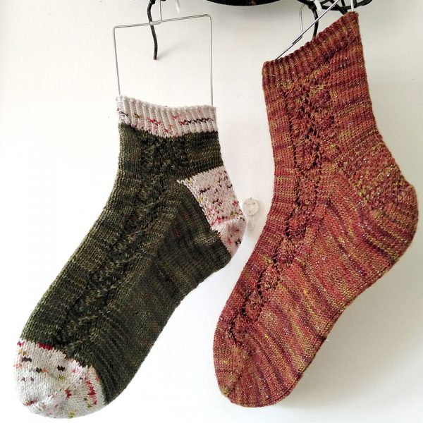 Two socks with a lace leaf pattern up the outside of the foot knitted in variegated brown yarn and green yarn with contrast toe, heel and cuff.