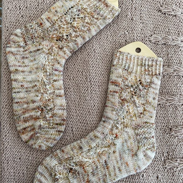 A pair of socks with a lace leaf pattern up the outside of the foot knitted in speckled cream and brown yarn