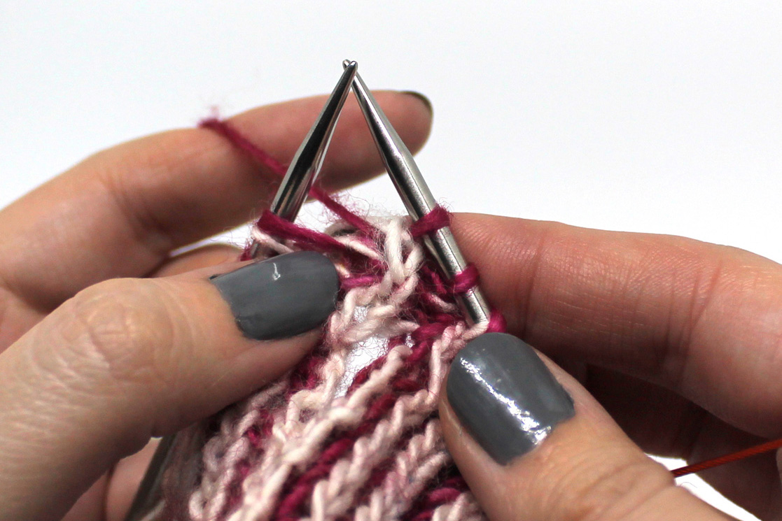 The second stitch on the right hand needle (in white) has been passed over the first stitch (in pink) and off the needle