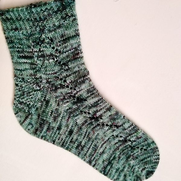 A Giuthas sock knit in green speckled yarn on a sock blocker