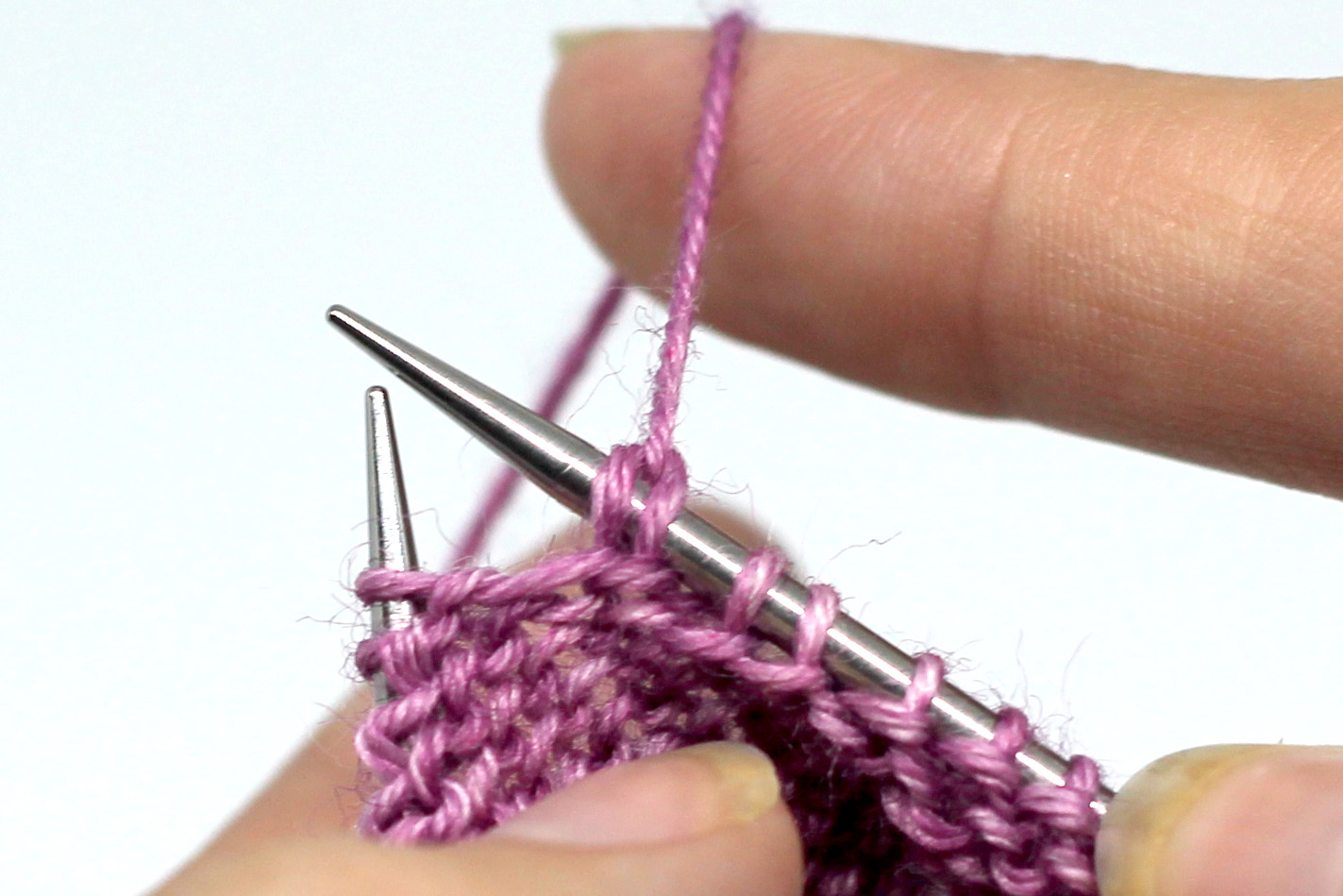The working yarn has been pulled up over the knitting needle, causing the stitch to change shape and giving two strands over the needle instead of one.