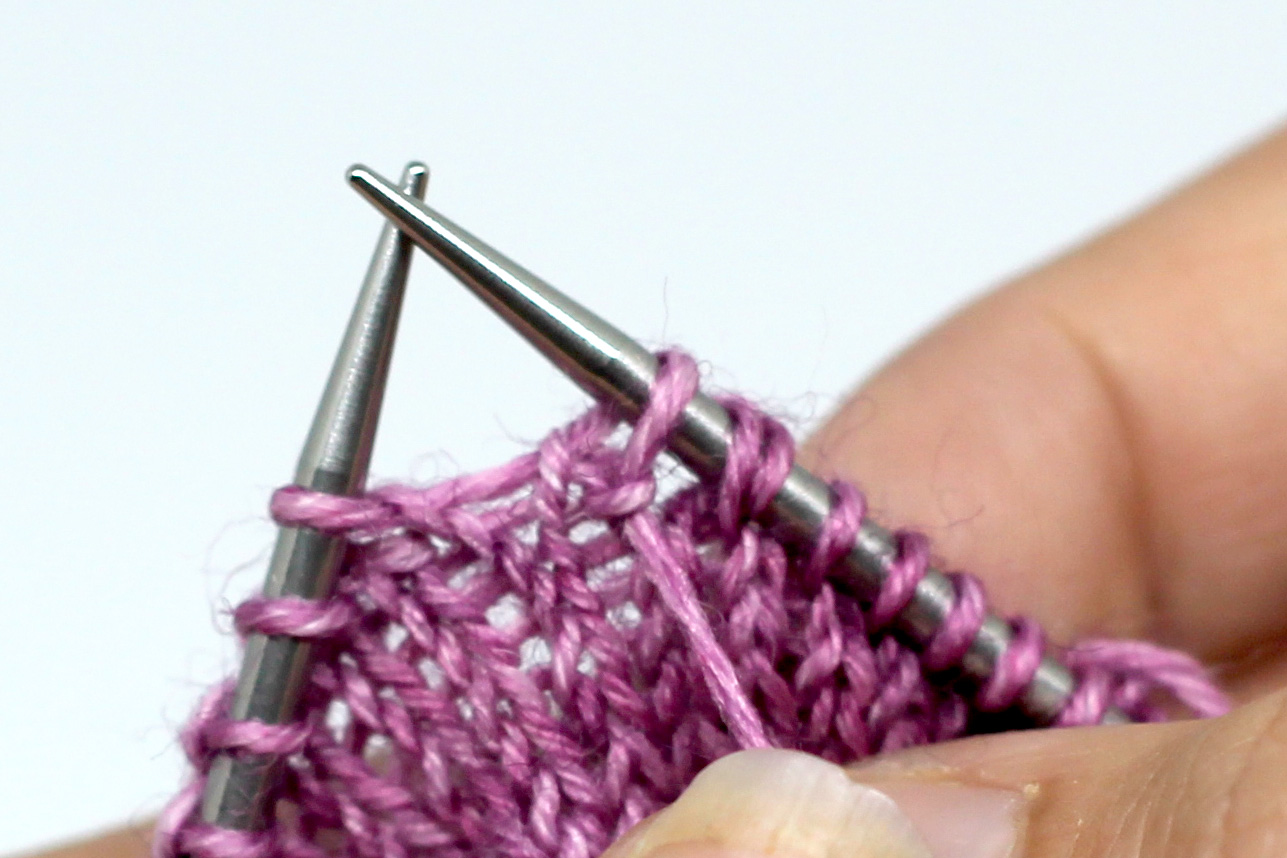 The working yarn has been brought to the front between the needles and the first stitch slipped from the left-hand needle to the right-hand needle