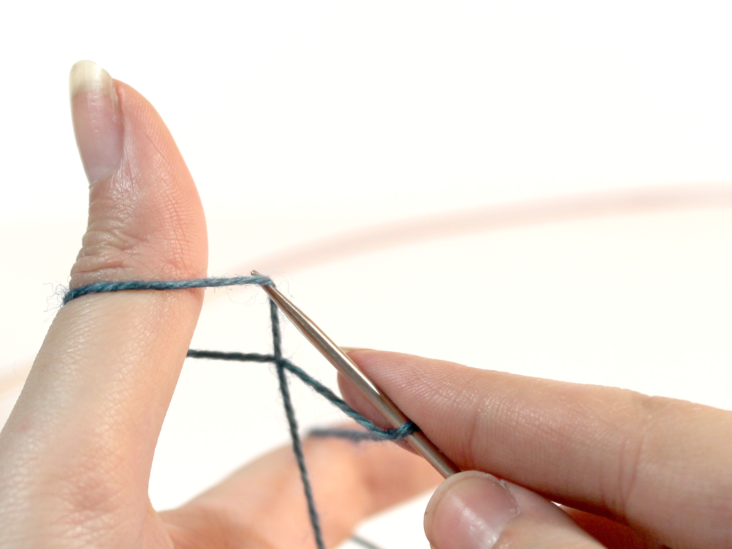 The knitting needle is lifting the strand of yarn that runs from the ring finger to the thumb on it's tip.