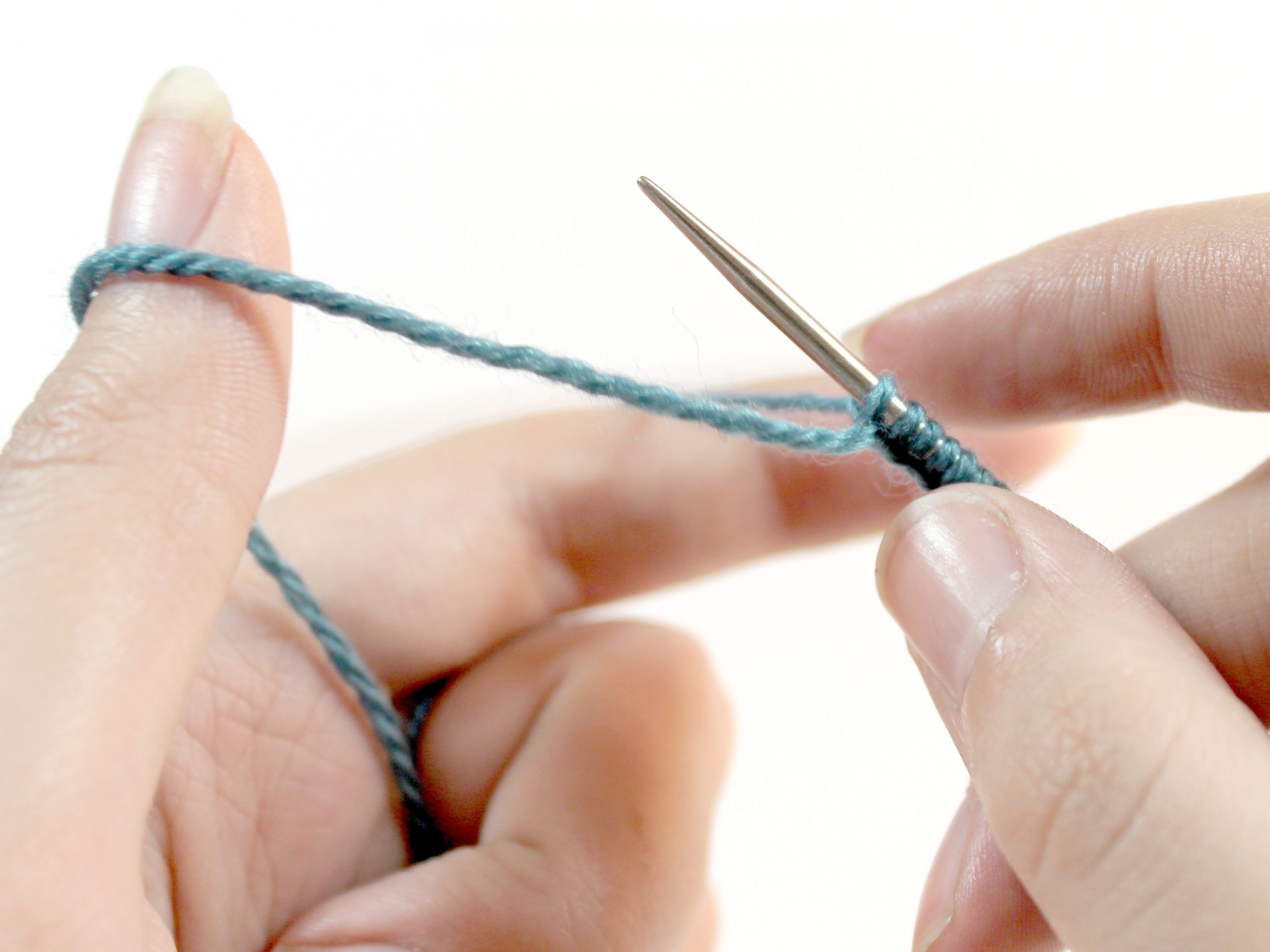 The knitting needle is ready for a new stitch. The yarn now runs from the knitting needle around the back of the thumb to the ring finger.