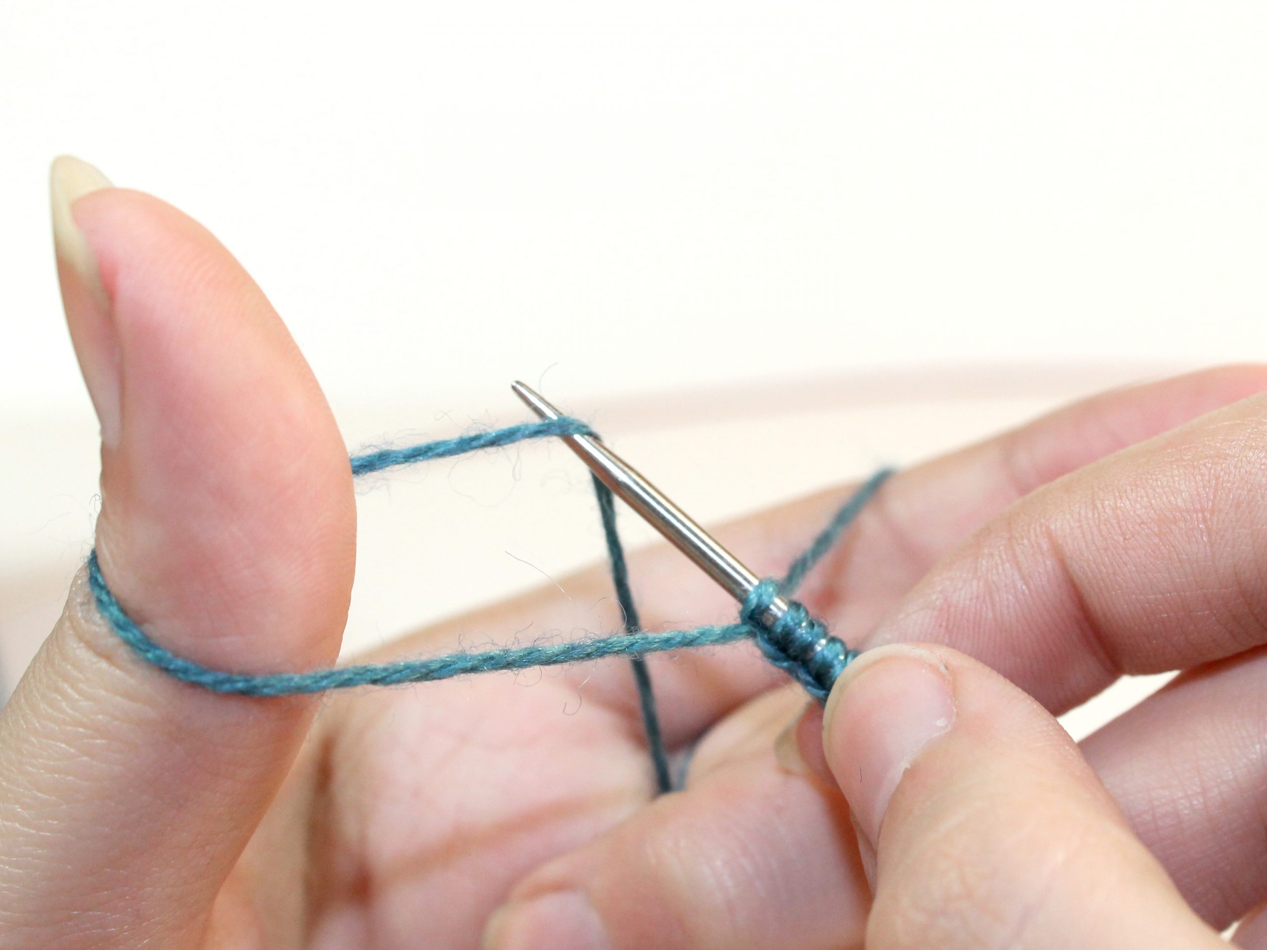 The needle tip lifts the yarn that rubs between the ring finger and thumb