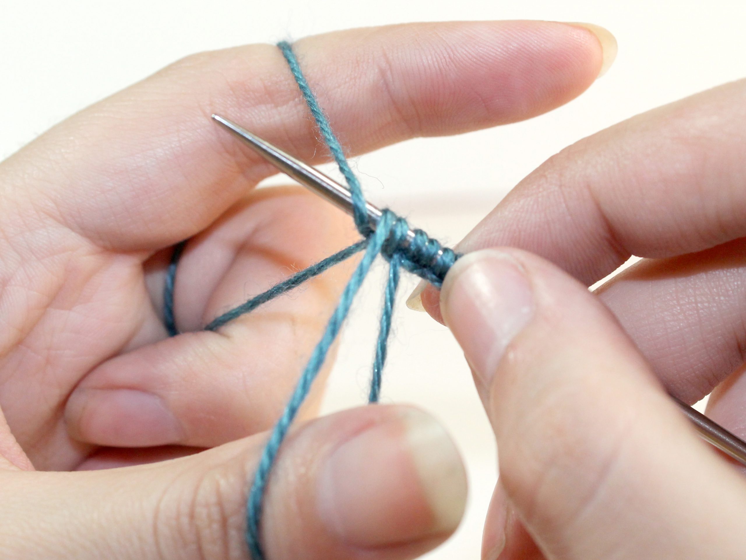 The knitting needle catches the yarn running from the knitting needle to the index finger