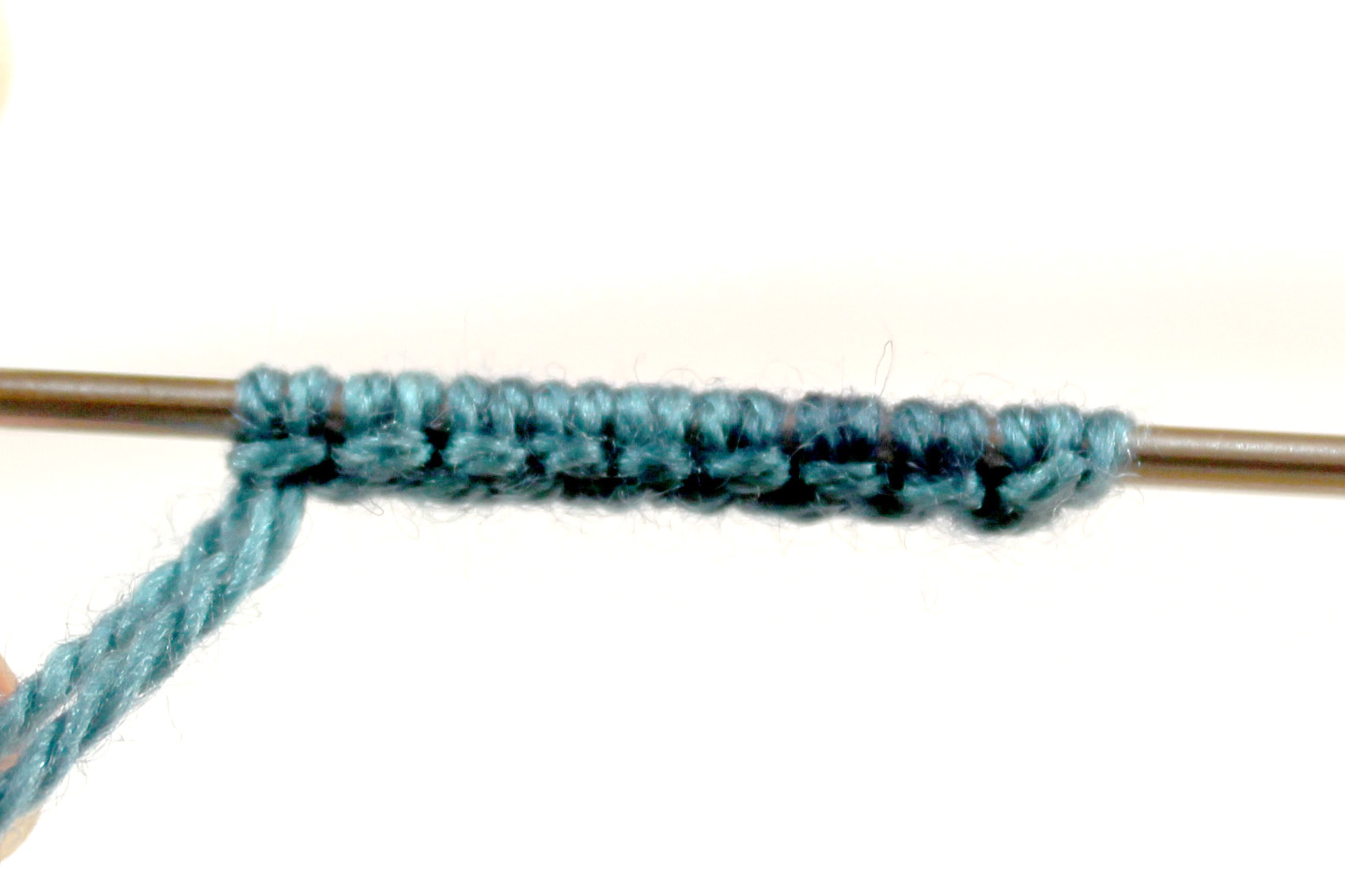 A cast-on on a needle with stitches arranged in pairs with a horizontal band of yarn wrapped around them.