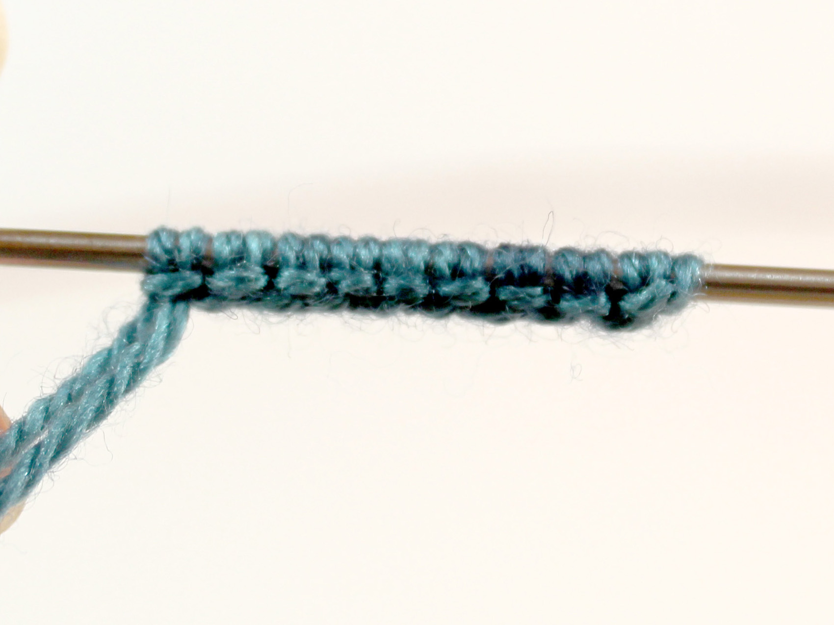 A cast-on on a needle with stitches arranged in pairs with a horizontal band of yarn wrapped around them.