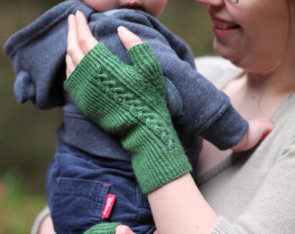 Twisted rib fingerless mitts with a large cable up the back of the hand and a narrow cable pattern that splits around the thumb (the model is holding a baby)