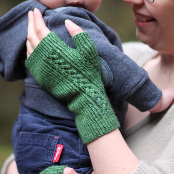 Twisted rib fingerless mitts with a large cable up the back of the hand and a narrow cable pattern that splits around the thumb (the model is holding a baby)