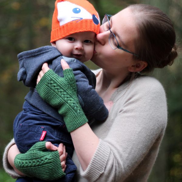 Twisted rib fingerless mitts with a large cable up the back of the hand and a narrow cable pattern that splits around the thumb (The model is holding a baby)