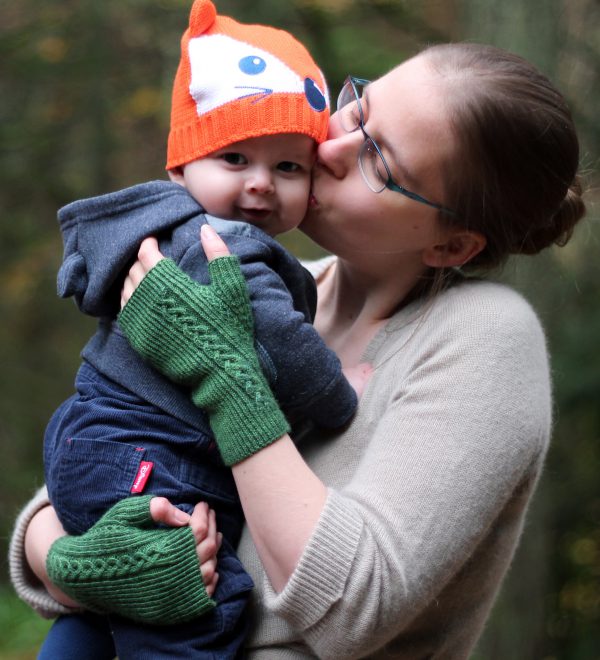 Twisted rib fingerless mitts with a large cable up the back of the hand and a narrow cable pattern that splits around the thumb (The model is holding a baby)