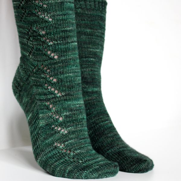 A modelled pair of socks in dark green with a lace pattern representing half a fir tree on the foot and a whole fir tree on the leg