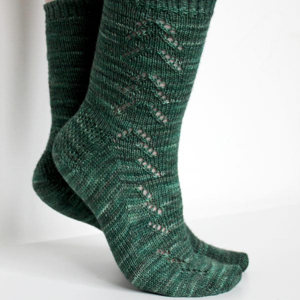 A modelled pair of socks in dark green with a lace pattern representing half a fir tree on the foot and a whole fir tree on the leg