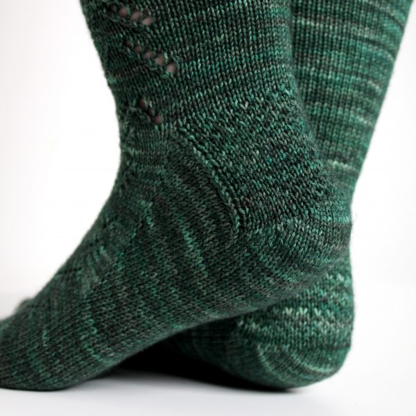 A close up on the textured heel pattern of a modelled pair of socks in knit dark green