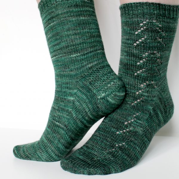 A close up on a sock knit in dark green with a lace pattern representing a whole fir tree on the leg